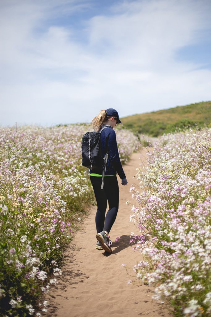 A woman hiking on a trail surrounded by wild flowers.