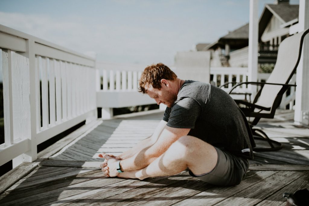 A man sits on a porch and stretches forward with feet together (Butterfly pose)